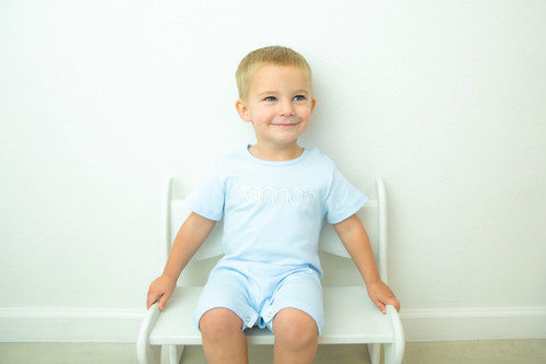 Toddler boy wearing a baby blue short sleeve knit romper with snap buttons on the legs and shoulder